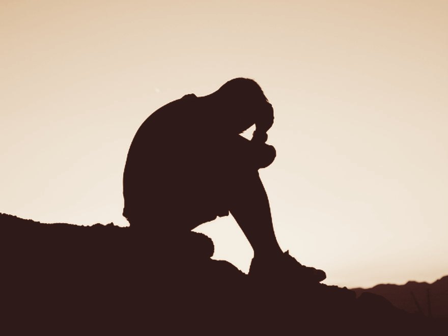 Ein Mensch sitzt allein auf einer Anhöhe