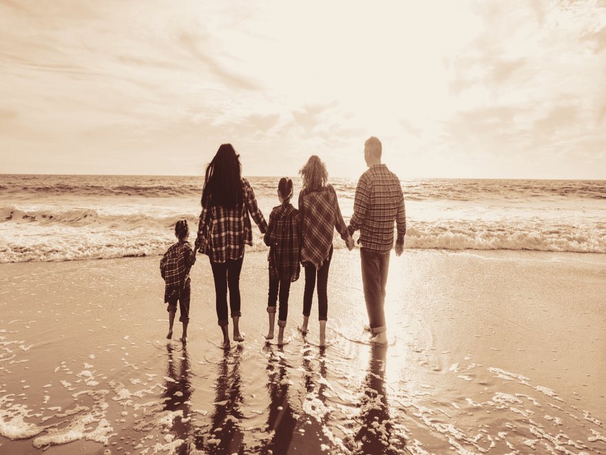 Eine Familie geht Hand in Hand am Strand ins Licht