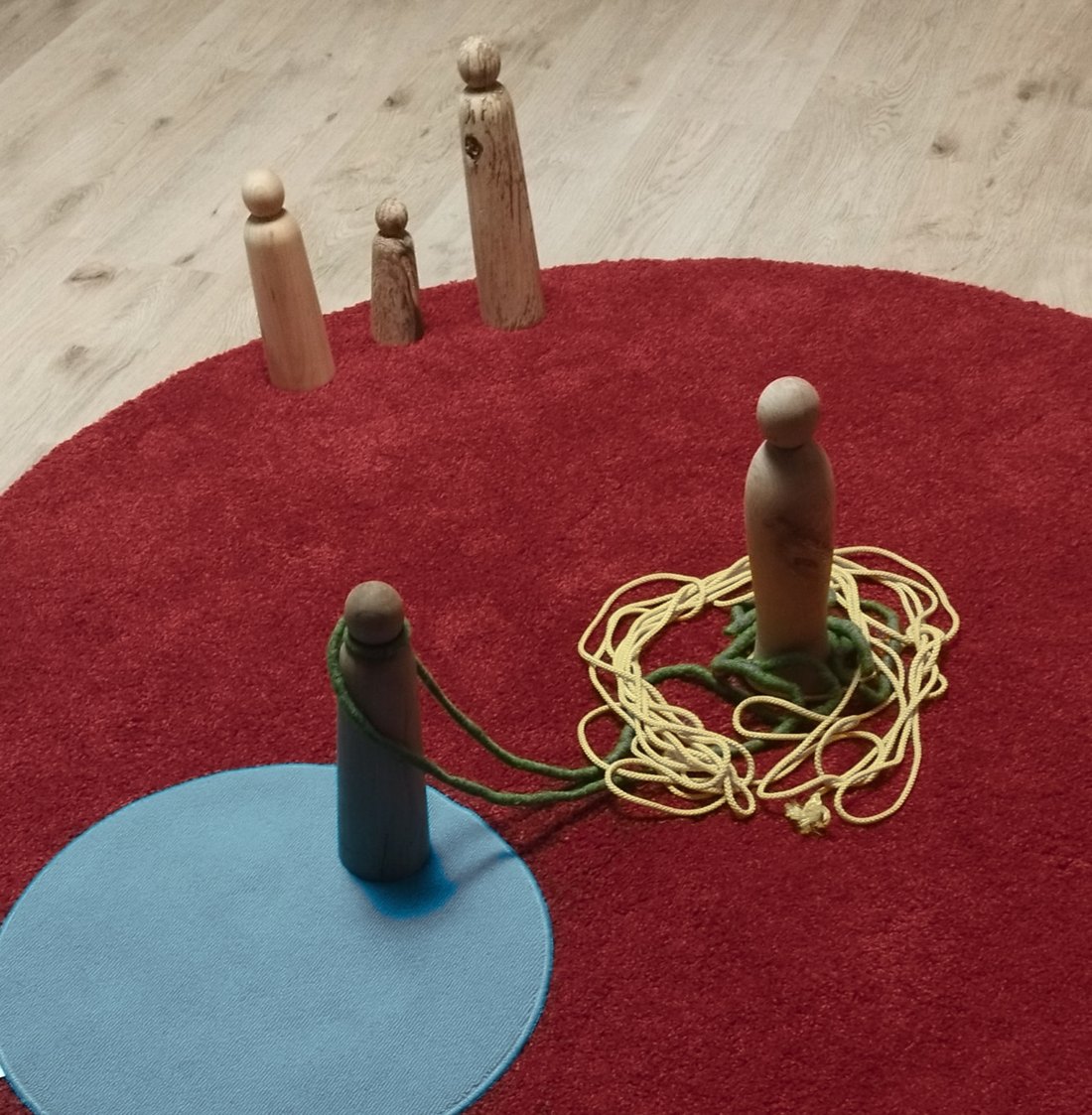 Holzfiguren auf einem Teppich, zwei davon mit Seilen verbunden