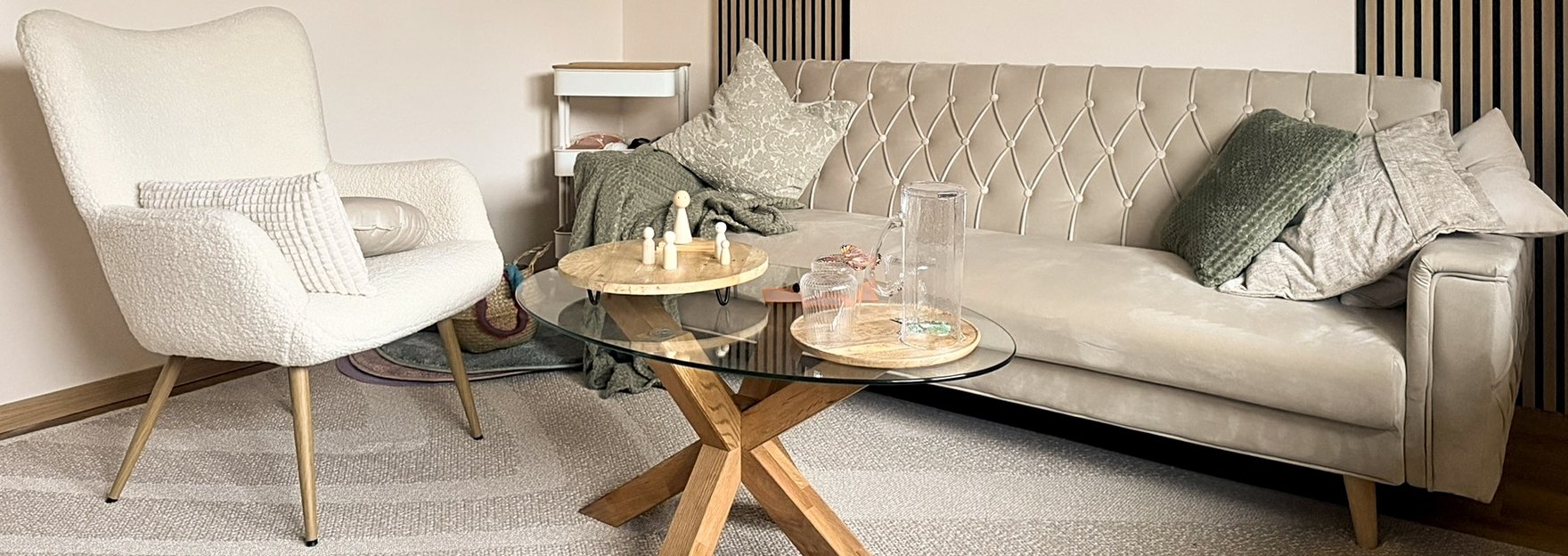 Der Praxisraum in Erlangen: Sessel, helles Sofa und ein Glastisch mit Holzfiguren und Wasserkaraffe
